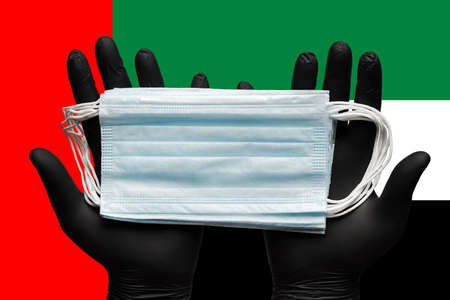 Doctor holds medical face mask in hands in black gloves on background colors national flag of United...