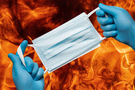 Paramedic holding lot medical face masks in hands in blue gloves on background flames of strong red...