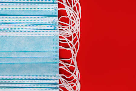 Surgical and medical face masks for coronaviruse on red background. Close-up view of lot respiratory face bandage with rubber ear straps. Copy space, concept protection, 2019-ncov, virus prevention.の写真素材
