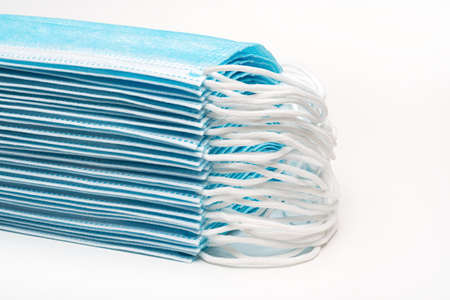 Stack blue surgical medical face masks with rubber ear straps on white background. Concept pandemic insurance coronavirus, SARS. Close-up view of respirator bandage for human face. Forced perspectiveの写真素材