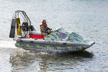 Man in camouflage uniforms and life jacket riding airboat along water surface. Inflatable rubber air...