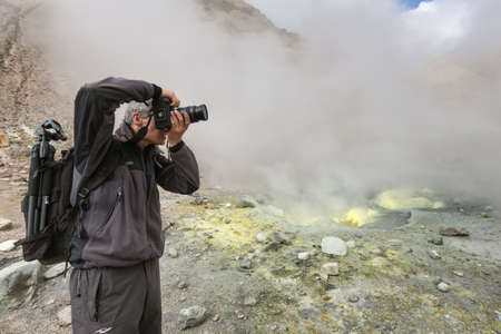 Male photographer takes pictures volcanic landscape, fumes aggressive hot springs, eruption...