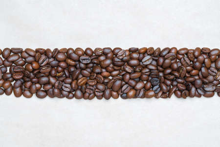 Brown coffee beans on background of light texture recycled eco-friendly paper. Central horizontal...