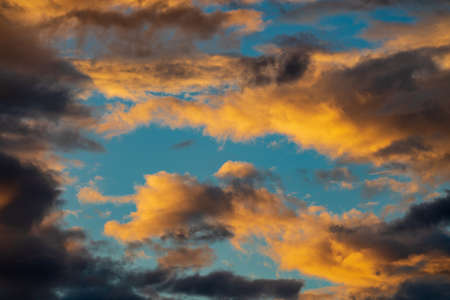 Dramatic fluffy clouds illuminated by disappearing rays at sunset, dark thunderclouds floating...