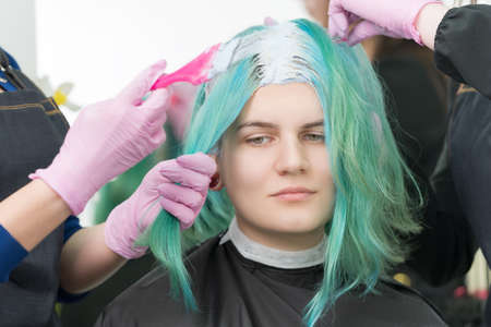 Process of bleaching hair roots in hair salon. Two hairdressers in protective glove use pink brush...