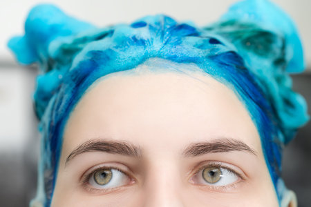 Close-up view of pretty girl with blue hair and big beautiful eyes with shampoo applied, while washing her hair after dyeing her sapphire hair in professional beauty salon.の写真素材