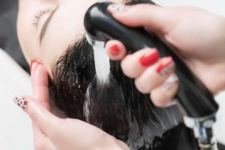 Hands of hairdresser wash long hair of brunette woman with shampoo, conditioner hair and shower water in special sink for shampooing in beauty salon.の写真素材