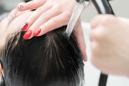 Hands of hairstylist wash long hair of brunette woman with shampoo in special professional sink for shampooing in beauty salon.の写真素材