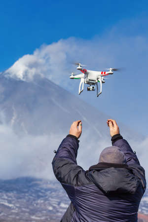 Male launches flying drone quadcopter UAV with digital camera on background of volcano eruption,...