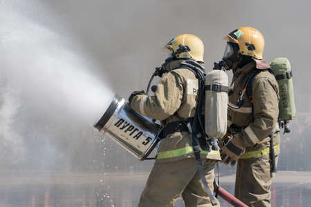 Firefighters extinguishes fire from fire hose, using fire-fighting water-foam barrel with air-mechanical foam during professional holiday Firefighters Day. Kamchatka Peninsula, Russia - April 27, 2019のeditorial素材