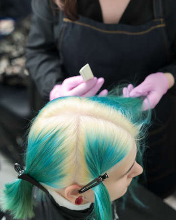 Top view of head of young woman with green hair and bleached hair roots, hair parting. Female in professional beauty salon before hair coloring process.の写真素材