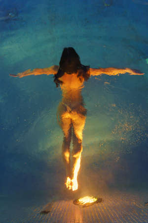 Woman with sports figure swims underwater in pool with thermal water illuminated by night lights....
