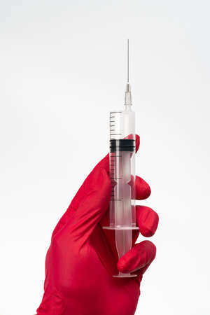 Doctor hands in red medical gloves holding medical syringe for vaccine injection on white background. Medical concept of immunization and vaccination campaign, single-use sterile medical devicesの写真素材