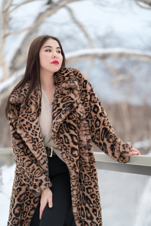 Three quarter view of brunette young woman with long hair in faux fur coat with leopard pattern and...