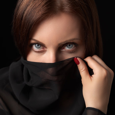 Portrait of shy woman covering her mouth and nose or face with scarf and looking at camera. Studio...