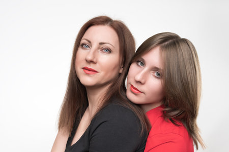 Portrait of woman mother and daughter looking at camera. Mom in black t-shirt and teenager in red t-shirt. Studio shot on white background. Part of photo seriesの写真素材