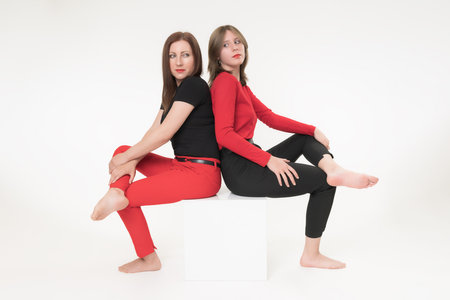 Woman mom and daughter sitting with their backs to each other on cube on white background. Both women crossed their legs and seriously looking over their shoulders at each other. Part of photo seriesの写真素材