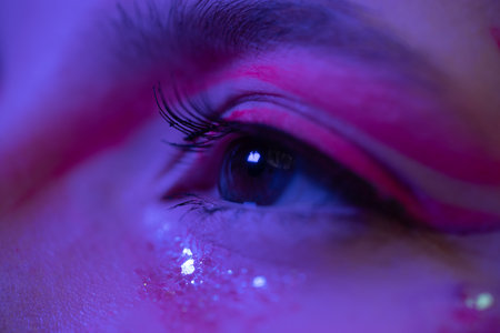 Extreme close-up view of women eye with shiny make-up with sparkles and arrows. Cinematic macro shot of female brown eye in neon light. Selective focus. Part of photo seriesの写真素材