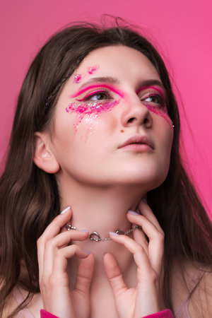 Close-up fine art portrait of young adult woman with pink stage make-up with sparkles and arrows painted on face. Beauty Caucasian ethnicity hipster female looking away. Studio shot on pink backgroundの写真素材