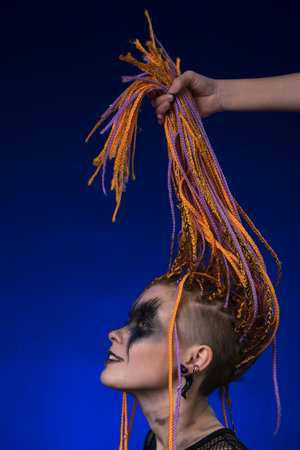 Fine art portrait of beautiful young female with orange color dreadlocks hairstyle and horror black...