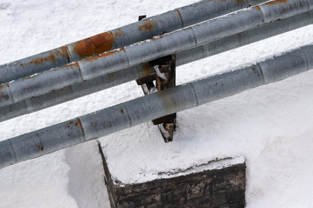 External city central heating pipes, with old rusty thermal insulation jackets, laid above ground. Pipes protected by rusty metal thermal insulation jacket. Pipes in winter, above snow after snowfallの写真素材