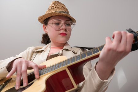Young female guitarist with glasses and straw hat is practicing classical six string acoustic guitar. Low angle view and dynamic perspective create an atmosphere, inspiring learningの写真素材