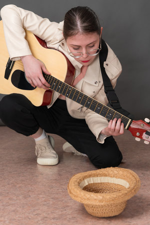 Female street musician strumming six string acoustic guitar for money and in front of her lying empty straw hat for donation for playing guitar. Woman standing on one knee while plucking instrumentの写真素材