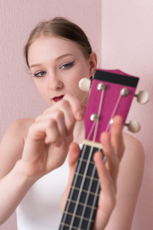 Young woman musician holding her ukulele and tuning strings of musical instrument, tightening and loosening strings before beginning to play ukulele. Daily routine ukulele tuningの写真素材