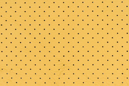 Yellow color abstract artificial leather with small dots and holes pattern for background. Close-up detail top view of sand colour breathable surface level simulated leather material for designの写真素材