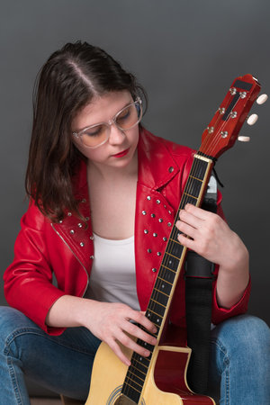 Female guitarist and musician in process of tuning her acoustic guitar, holding it upright and plucking strings in order to ascertain sound of her preferred musical instrumentの写真素材