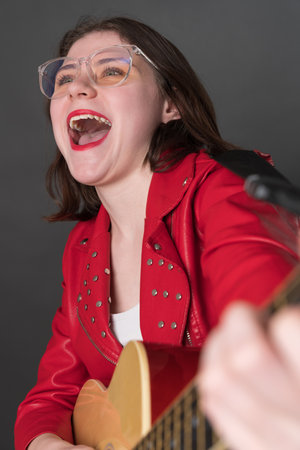 Happy young woman guitarist in state of pure joy playing classical guitar with passion, her mouth wide open, voice resonating with powerful emotion as she belts out song that hits right in heartの写真素材