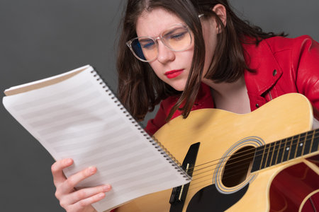 Close-up view of female guitarist in glasses carefully studying sheet music as she is learning to play classical six string acoustic guitarの写真素材