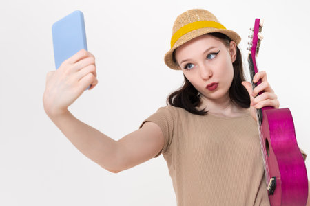 Musician and blogger posing in front of cell phone with ukulele in hand. Woman takes selfie, filming...