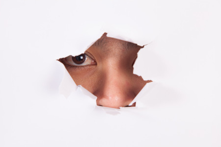 young girl peeping through hole in white paperの写真素材