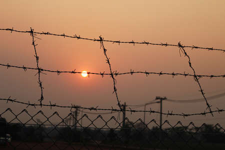 Fence with a barbed wire and sunsetの写真素材