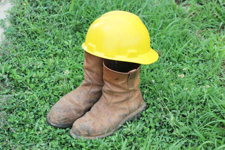 Old brown work boots and hard hat  on green grassの写真素材