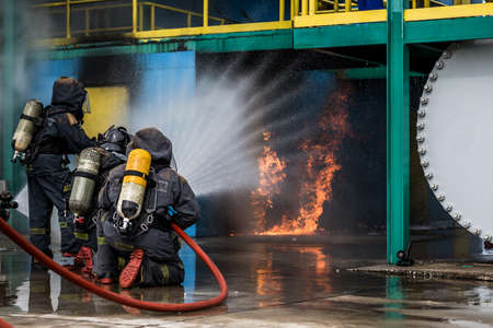 Firemen using water from hose for fire fighting at firefight training of insurance group. Firefighter wearing a fire suit for safety under the danger case.の写真素材
