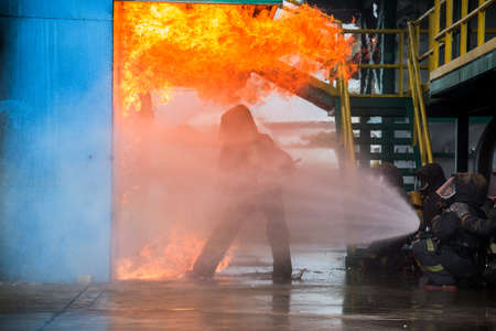 Firemen using water from hose for fire fighting at firefight training of insurance group. Firefighter wearing a fire suit for safety under the danger case.の写真素材