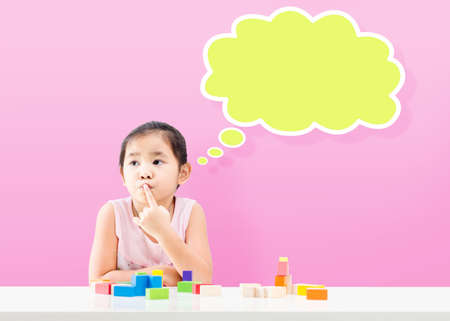 Thinking little girl with empty bubble and wooden building blocks on tableの写真素材