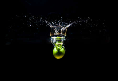 Green damson dropped into water with splash isolated on black backgroundの写真素材