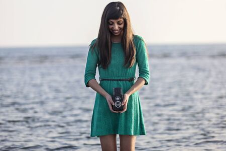 Vintage photo, brunette girl with retro camera by the seaの写真素材