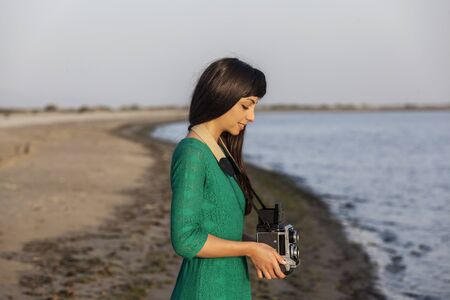 Vintage photo, brunette girl with retro camera by the sea
