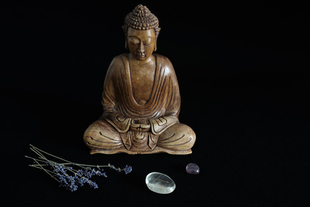 Wooden buddha statue with crystals and lavender on black background
