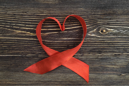 A red ribbon shaping heart , isolated on wooden backgroundの写真素材