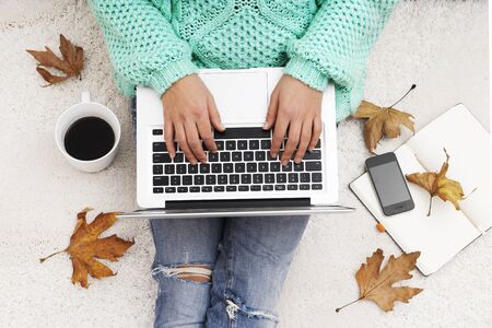 Laptop, smartphone,notebook and a cup of coffee in girl's hands sitting on a white carpet, top view