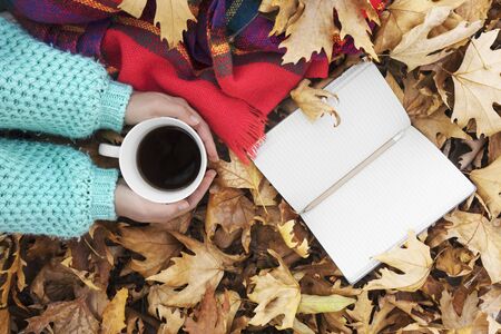 Woman hands holding cup of coffee over leaves background. top view