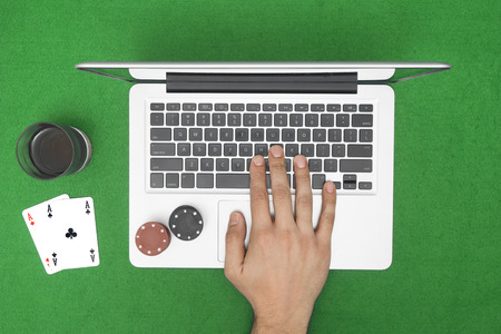 Man playing online poker with laptop on a green table with chips, top view