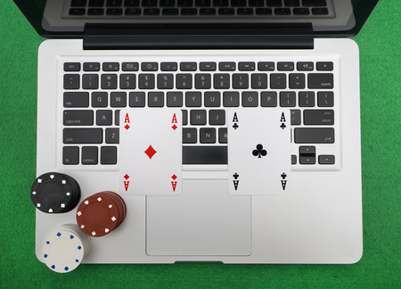 Laptop, poker cards and poker chips, on green background.top view