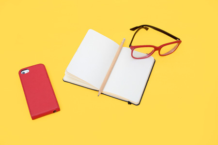 Eyeglasses, smartphone and notebook isolated on yellow background