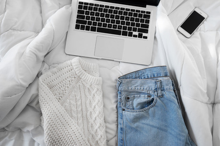 Female outfit, a  smartphone and a laptop laid out on bed, morning light
